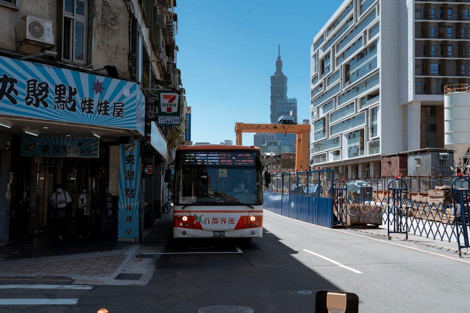 Bustling street in Taipei featuring public transport, construction, and Taipei 101 under clear blue skies.
