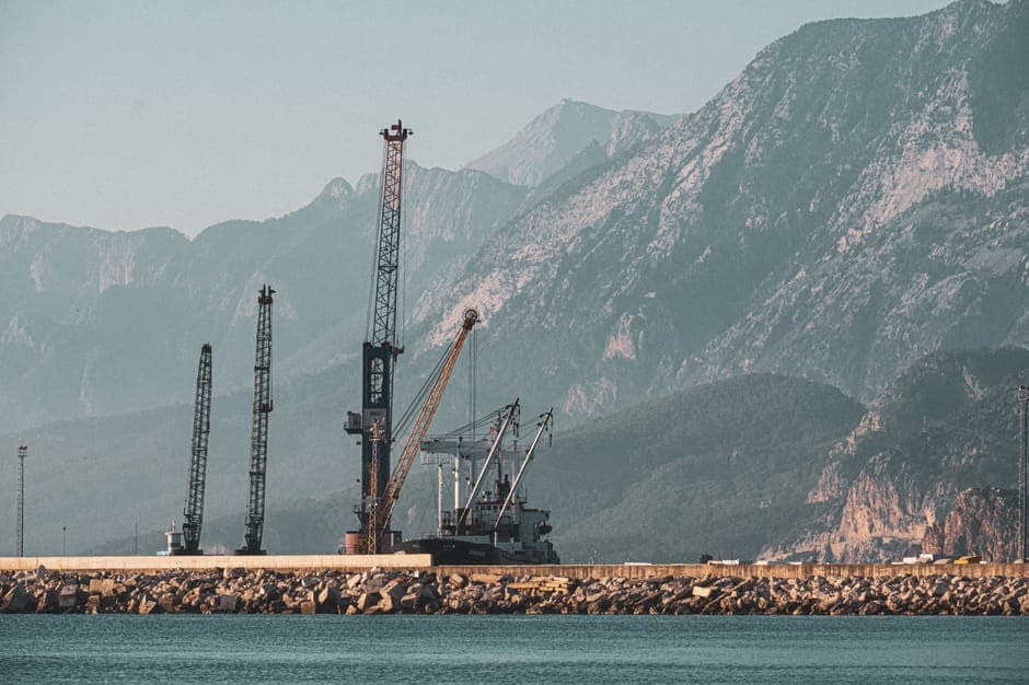 A serene harbor featuring cranes against majestic mountains on a clear day.