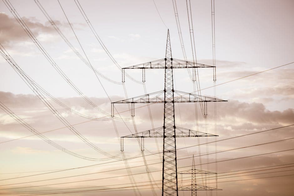 Silhouetted electricity pylons and power lines against a dramatic sky at sunset.
