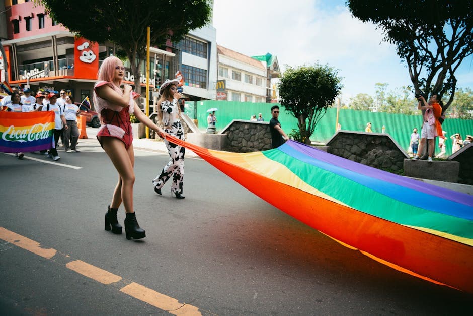 Colorful city parade showcasing pride with participants carrying a large rainbow flag.