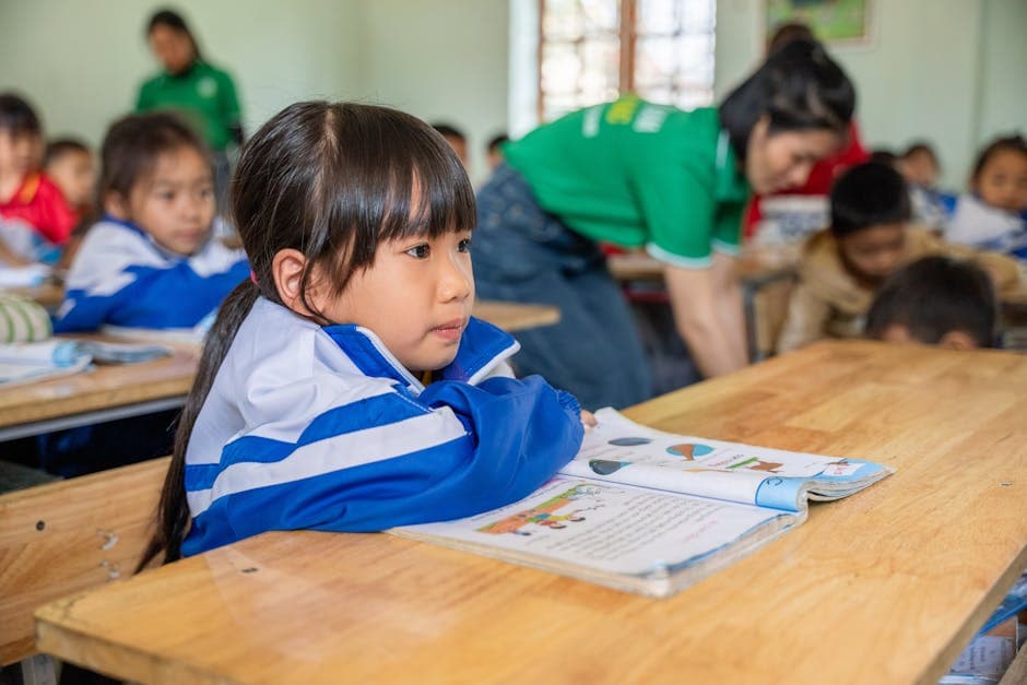 A focused young girl studying in an elementary classroom, seated among attentive peers.