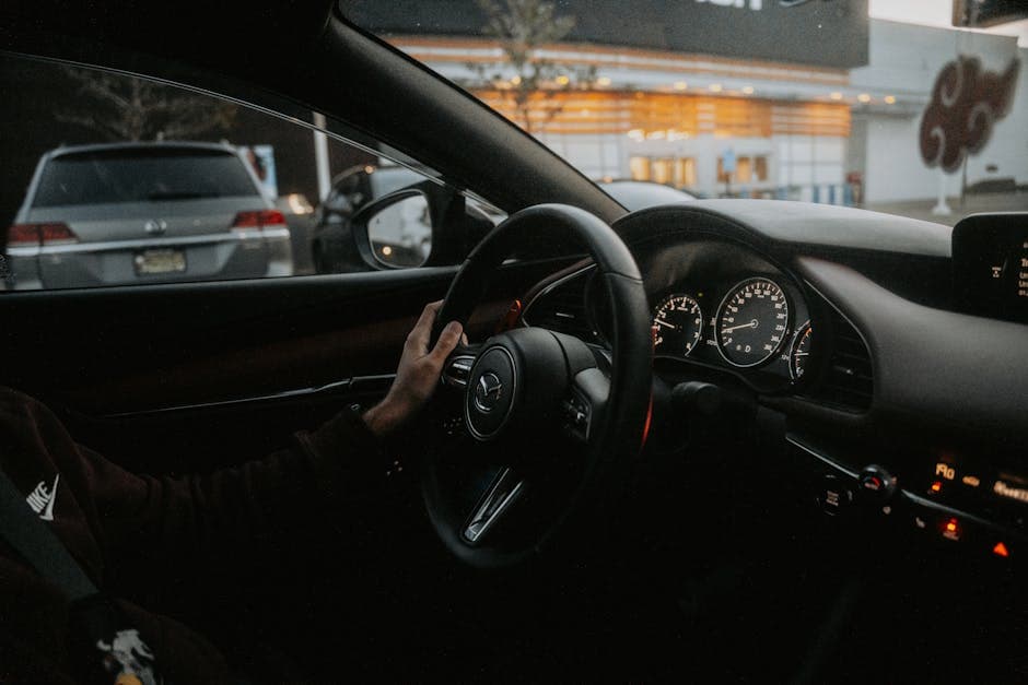 View from inside a car driving through a city at night, showing dashboard and steering wheel.