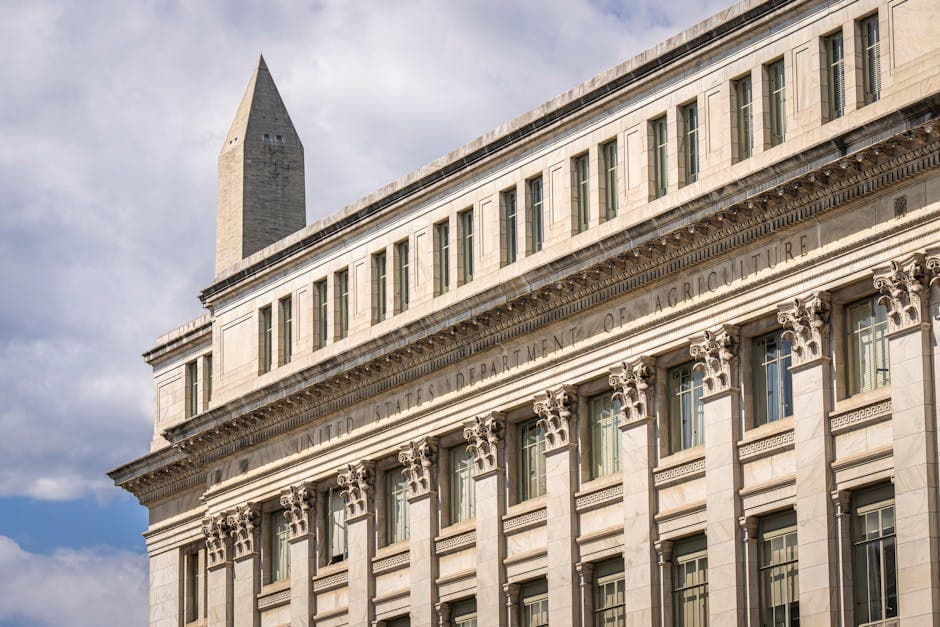 US Department of Agriculture building with Washington Monument behind, blue sky with clouds.