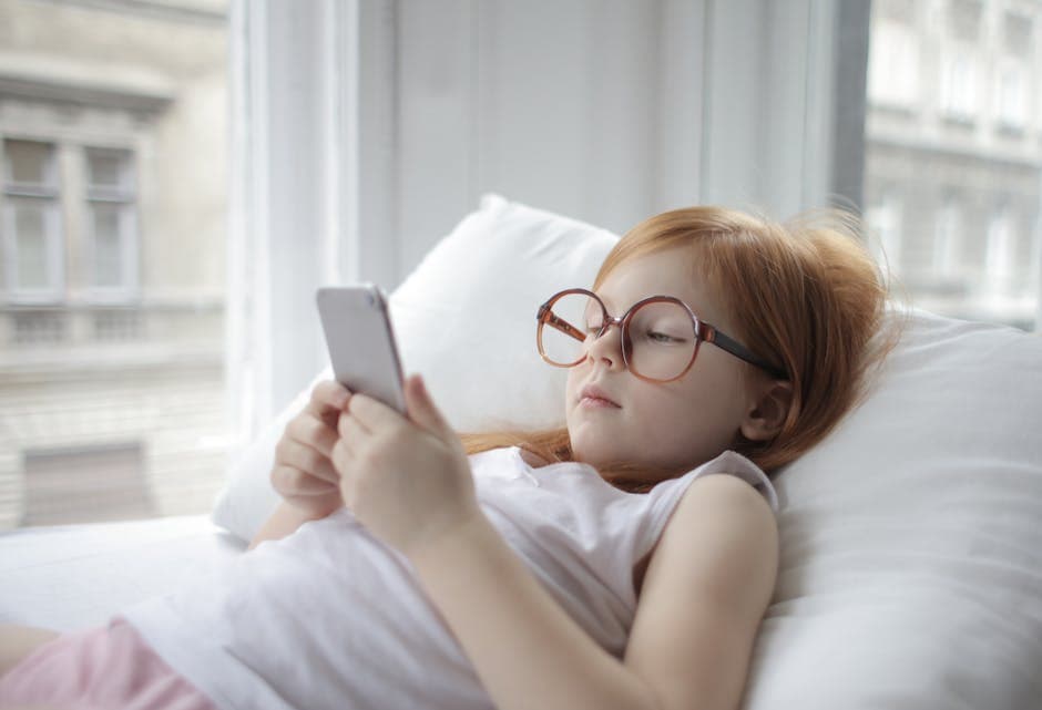 Girl relaxing indoors with a smartphone, showcasing modern childhood leisure.