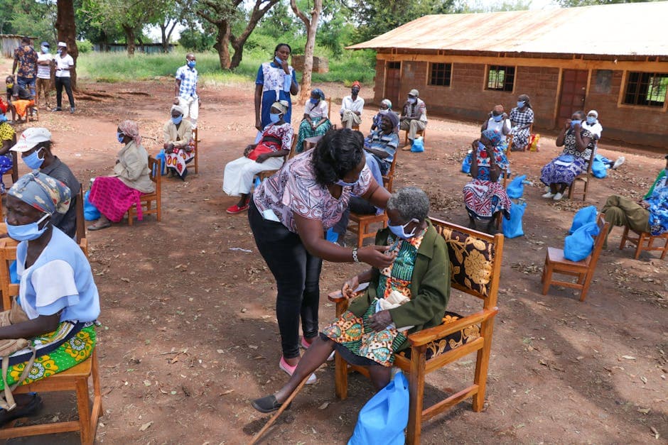 High angle of anonymous African female taking care of senior people in face masks sitting on chair near shabby building of nursing home in village