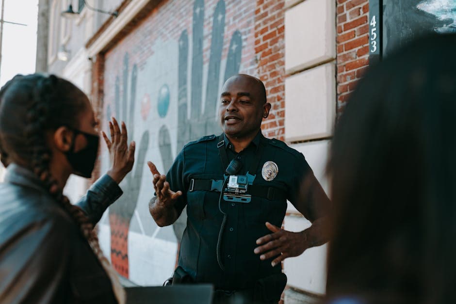 Police officer conversing with people on the street near a brick wall mural.
