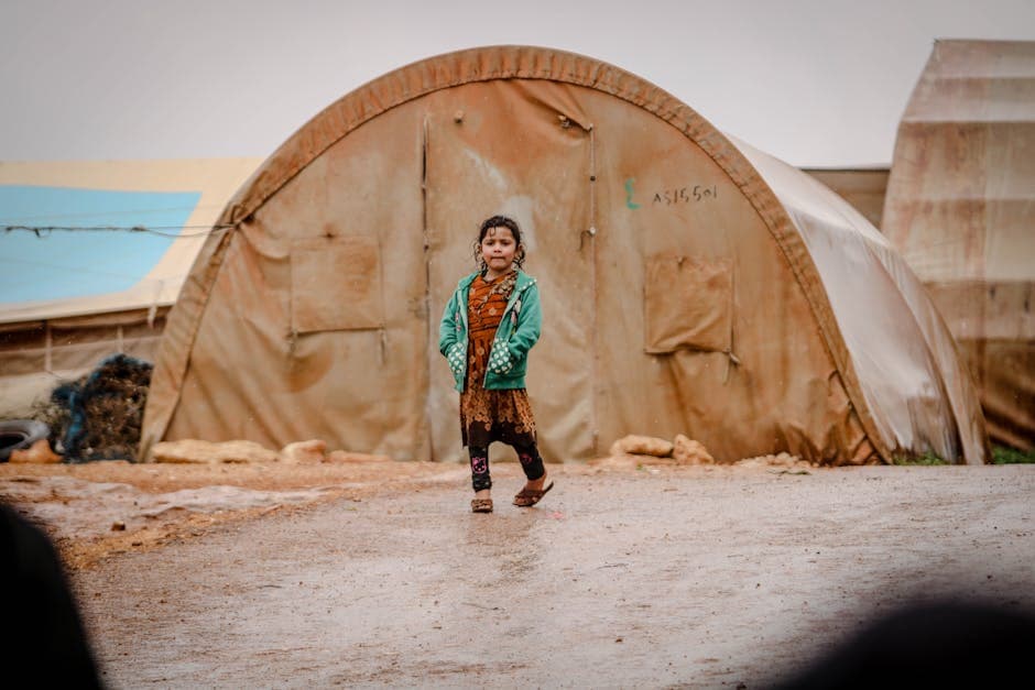 A young girl in a green jacket walks in a refugee camp in Idlib, Syria.