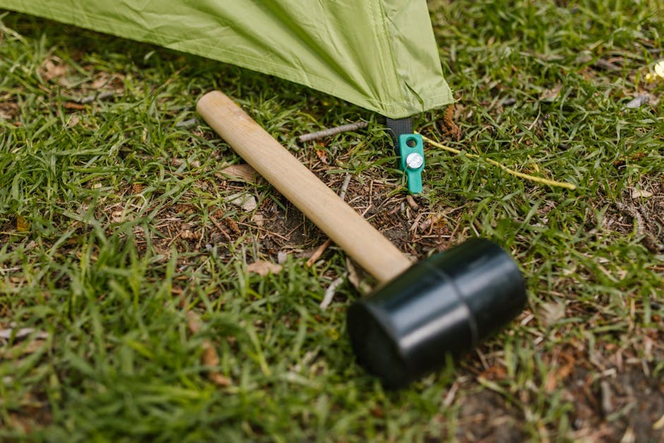 Close-up of a rubber mallet next to a green tent pegged on grass.