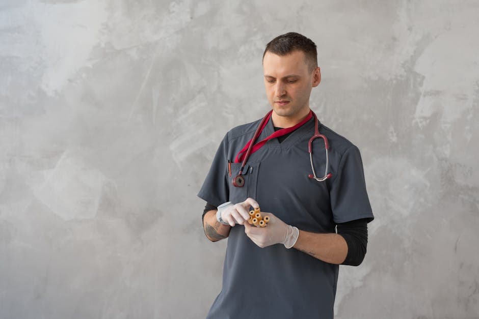 Male healthcare worker in gray scrub suit examining test tubes in a clinical setting.