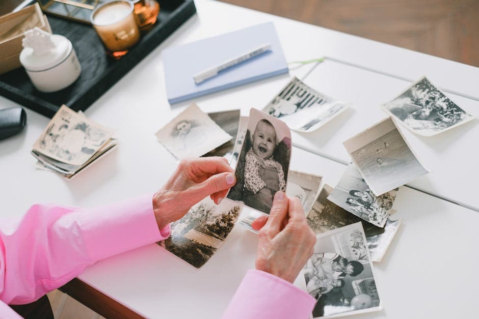 A person in a pink shirt organizing old black and white family photos on a table.