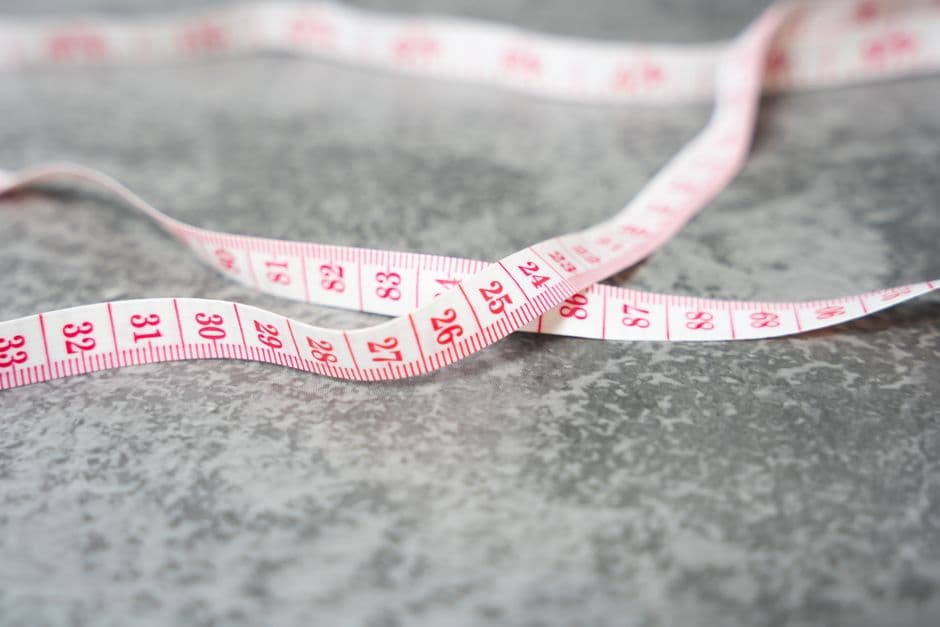 A detailed close-up of a measuring tape with pink numbers on a gray textured surface.