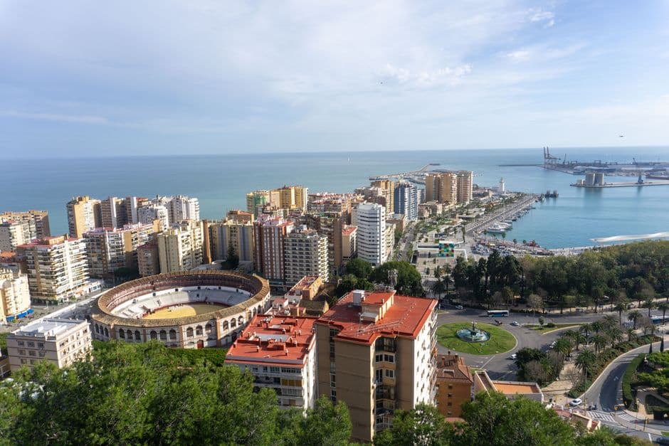 Stunning aerial view of Málaga's cityscape with a prominent bullring and picturesque coastline under clear skies.