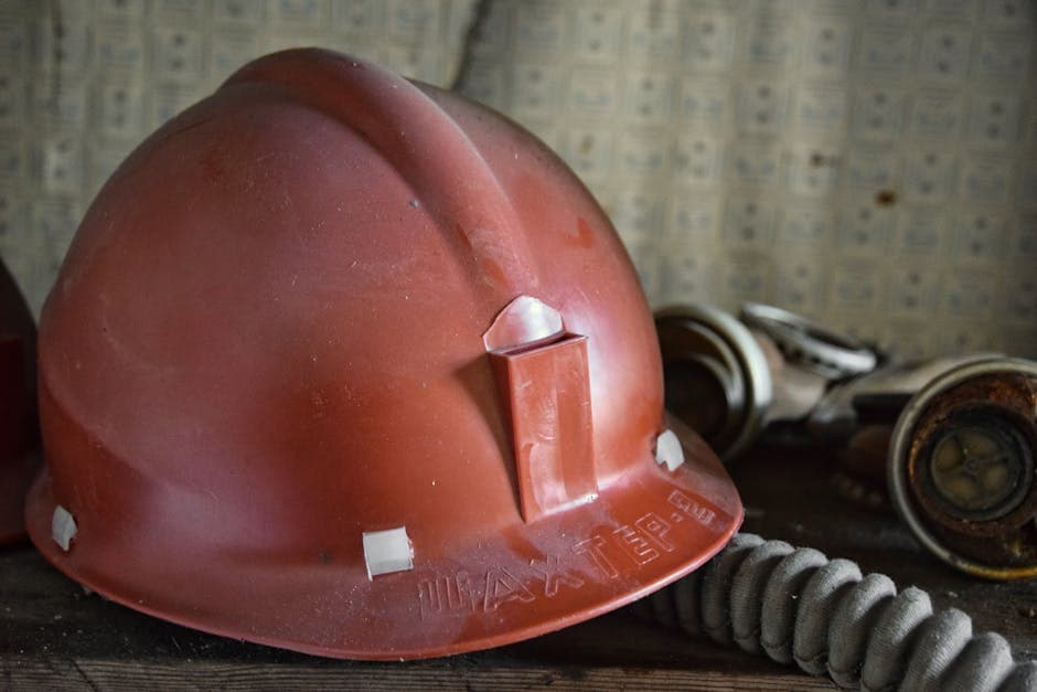 Close-up of a red safety helmet and filter mask in an industrial setting.