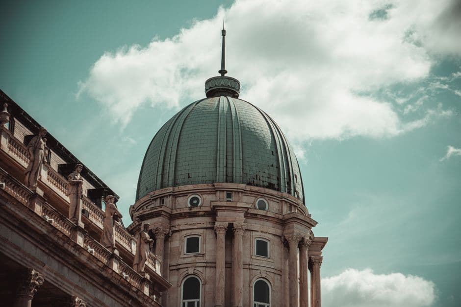 Elegant architectural dome with statues under a cloudy blue sky in Budapest, Hungary.