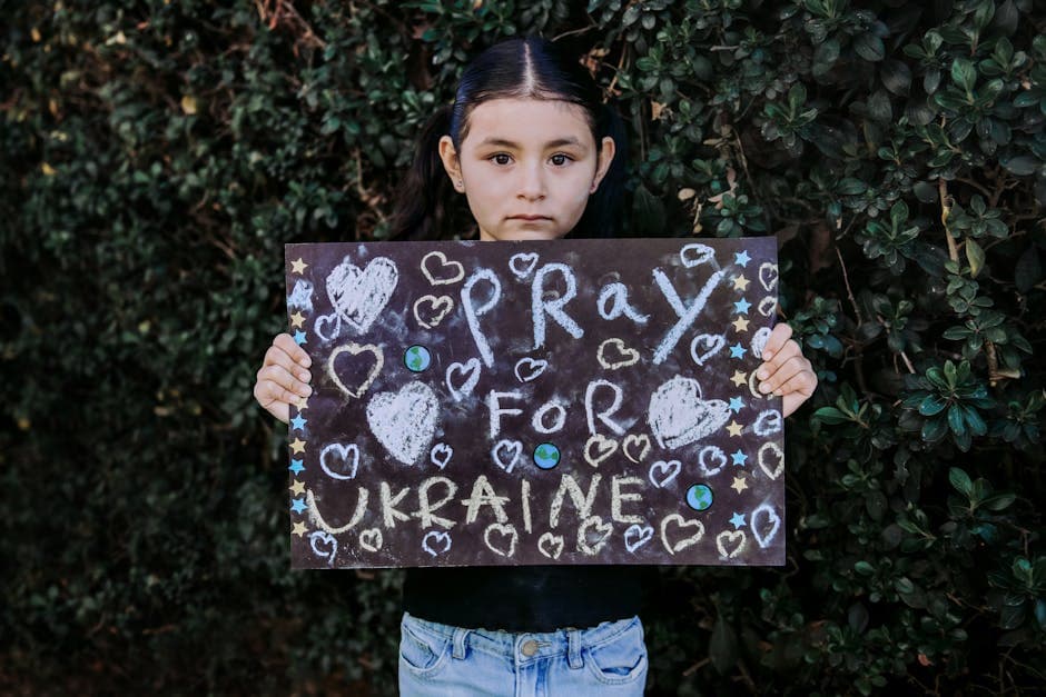 A young girl holds a chalkboard with 'Pray for Ukraine' message surrounded by hearts, promoting peace.