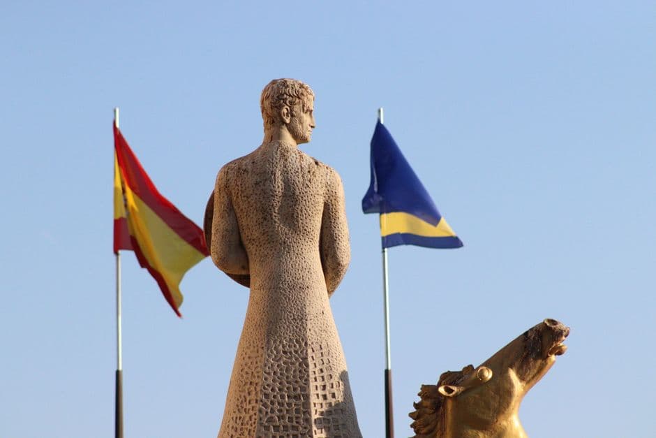 A statue facing two flags, one Spanish, against a clear blue sky in Salou.