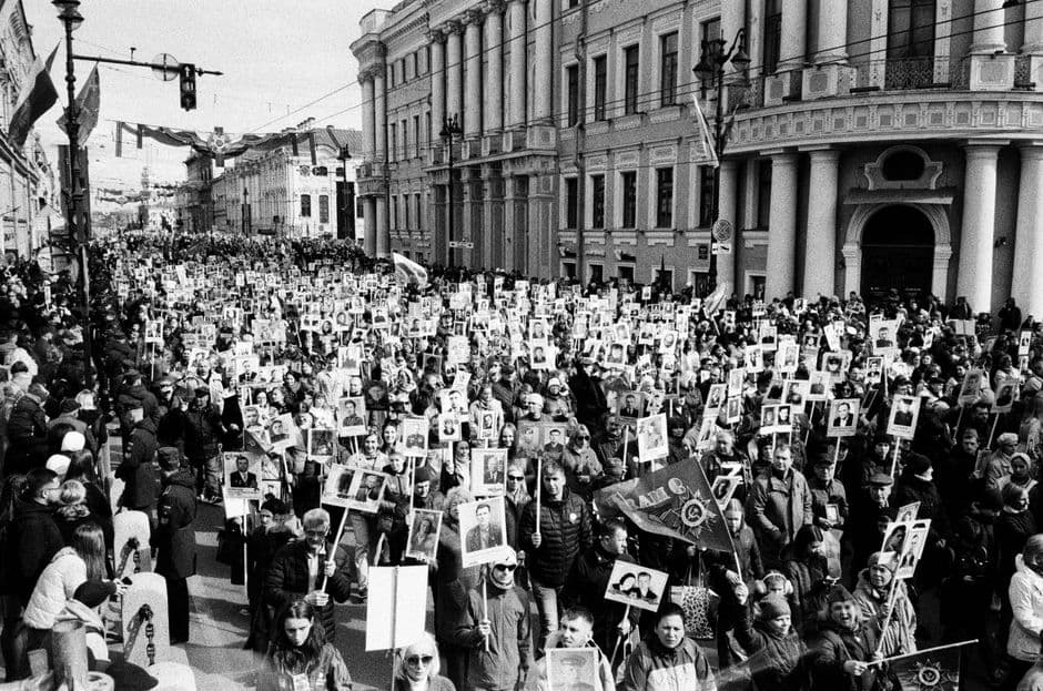 A black and white image of a large crowd of protesters holding signs during a daylight rally on a city street.