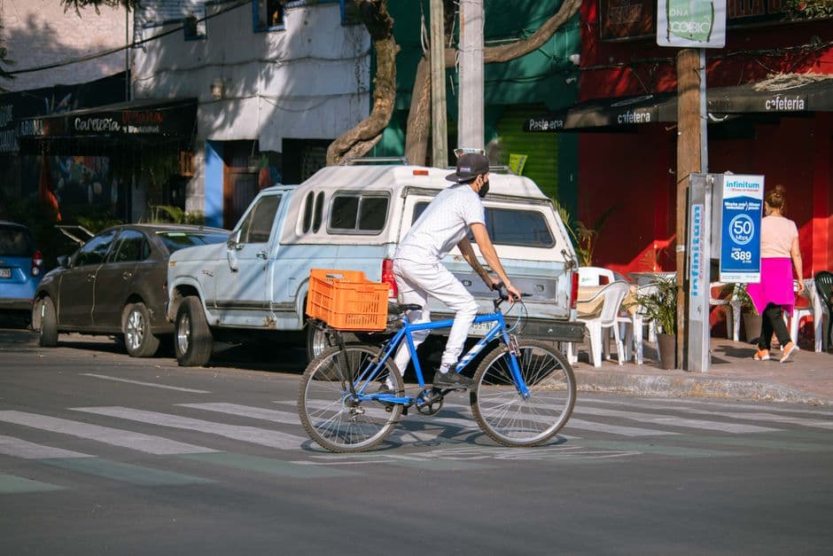 A man wearing a mask rides a bicycle across a busy street in an urban setting.