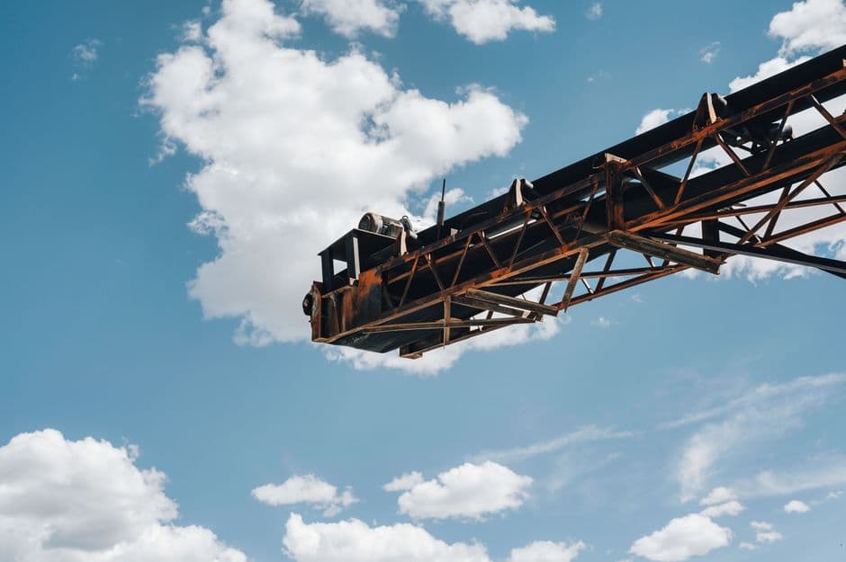 Close-up view of a rusty industrial crane framed against a clear blue sky with scattered clouds.