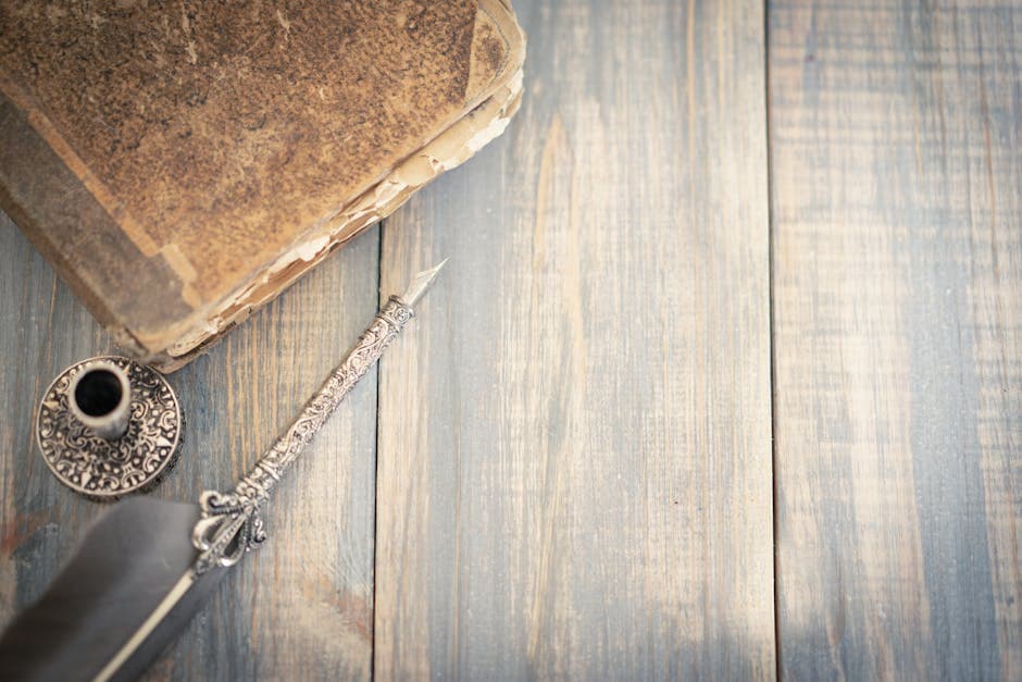 An overhead shot of a vintage book, ornate quill pen, and ink holder on a rustic wooden surface.