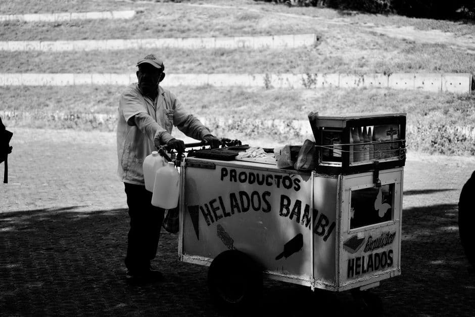 Monochrome image of a traditional ice cream vendor with a classic cart on a street.