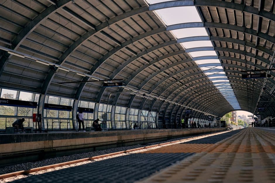 Modern railway station platform with curved steel roof and waiting passengers.