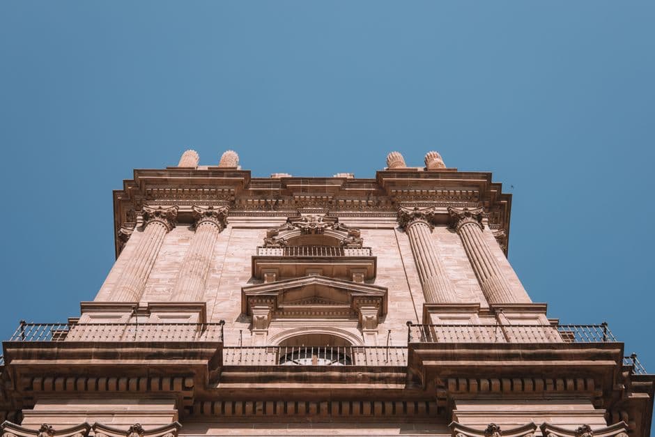 Low angle view of Málaga Cathedral's ornate facade, highlighting its architectural beauty against a bright blue sky.