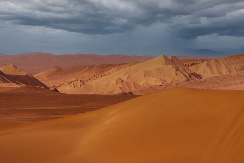 Stunning desert sand dunes under stormy skies capturing the raw beauty of arid landscapes.