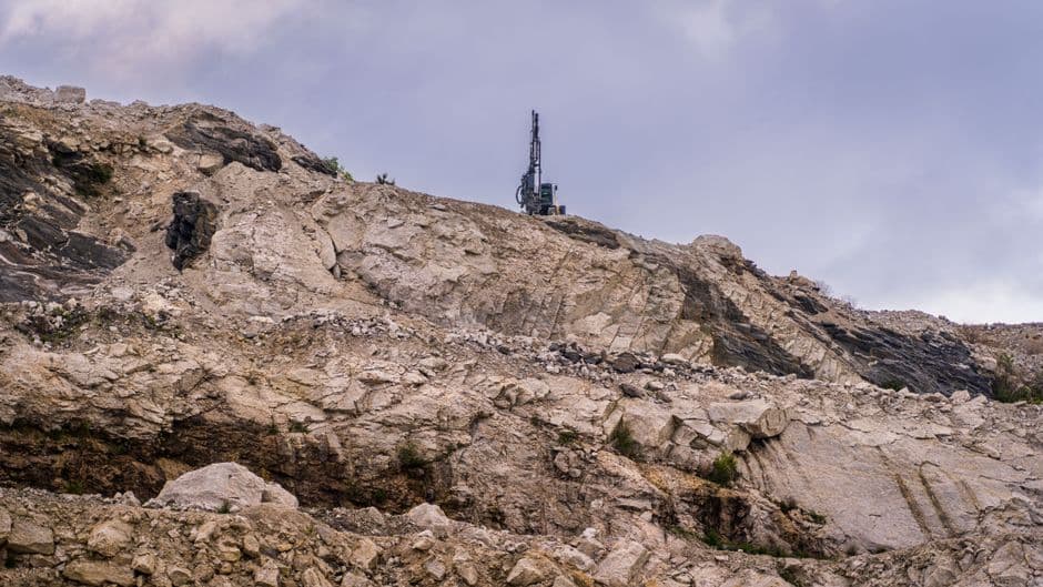 Rocky quarry site with visible erosion and industrial machinery against an overcast sky.