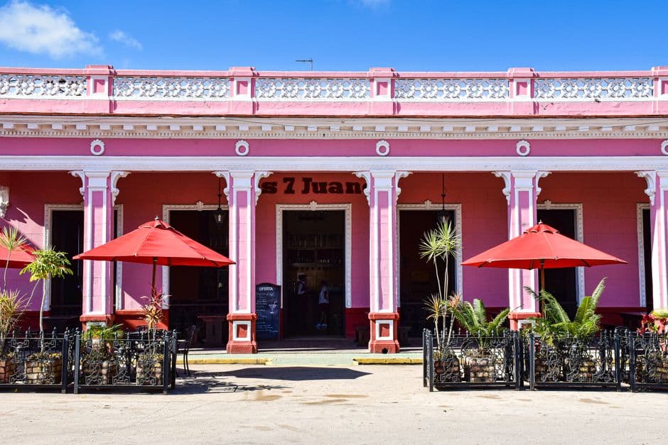 Sunlit pink café with red umbrellas in Remedios, Cuba, showcasing colorful colonial architecture.
