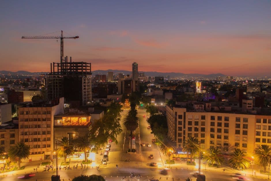 Aerial view of Mexico City's illuminated skyline at twilight, showcasing urban life and architecture.