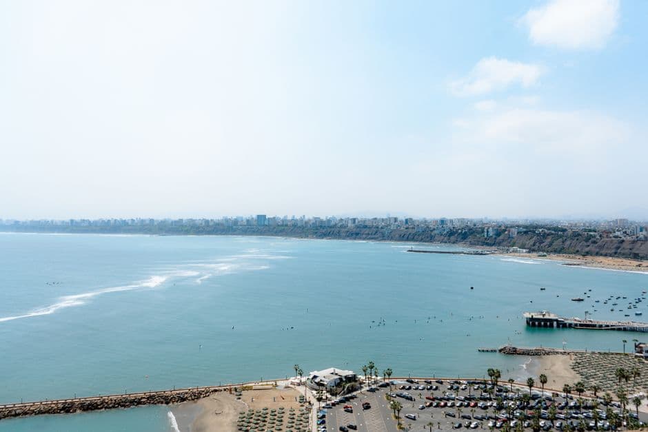 Aerial perspective of a coastal cityscape with a sandy beach, blue sea, and urban skyline under a clear blue sky.