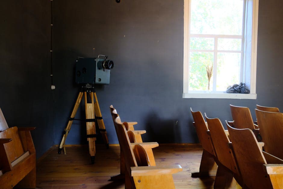Empty vintage room with a classic projector and wooden chairs by a bright window.