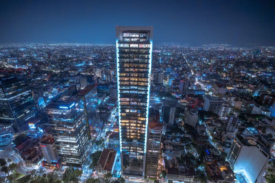 Aerial night view of Mexico City's illuminated skyscrapers and sprawling urban landscape.