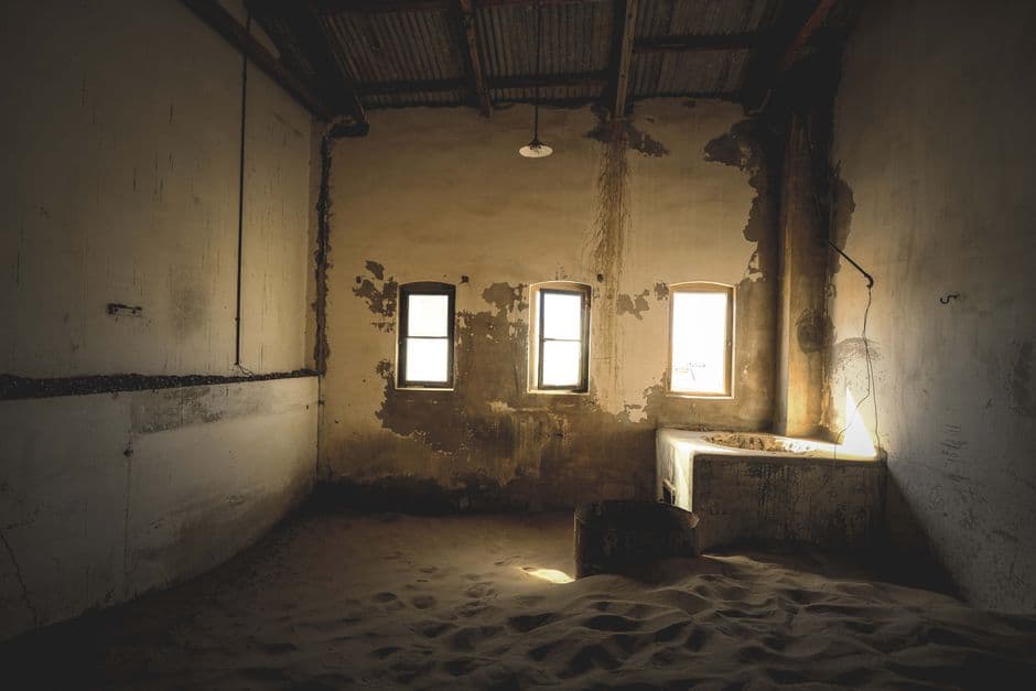 Eerie, abandoned room filled with sand, showcasing decay and vintage architecture.