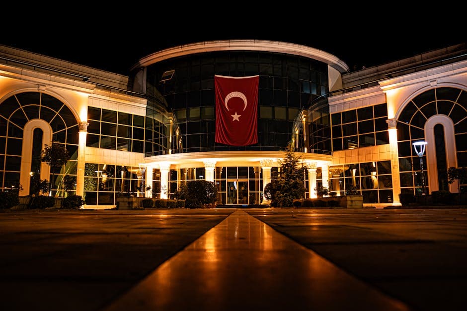 Illuminated modern building with Turkish flag at night, showcasing architecture.