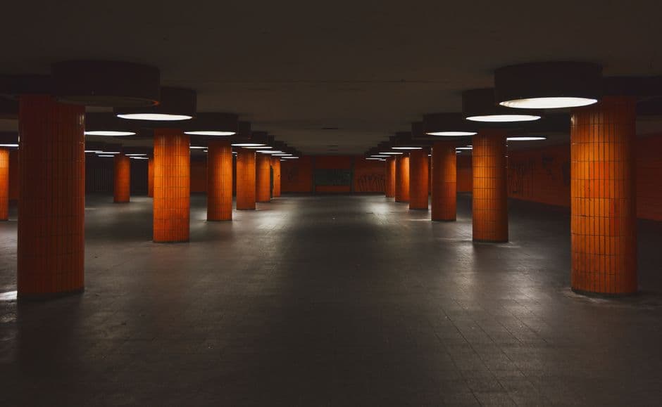 A dimly lit subway station with orange-tiled columns and circular lights, creating a moody atmosphere.