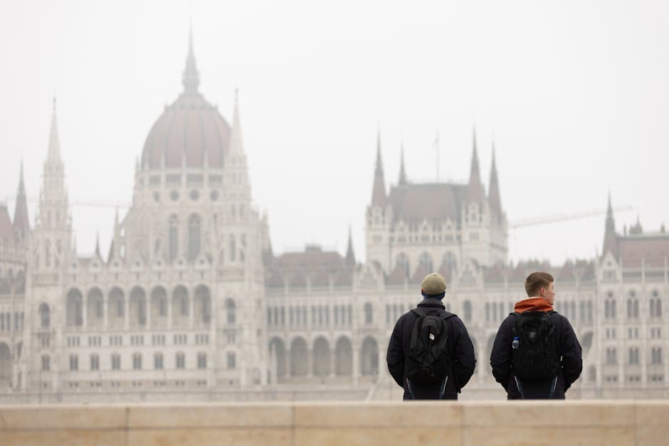 Two tourists with backpacks admire the Hungarian Parliament Building in Budapest on a foggy day.