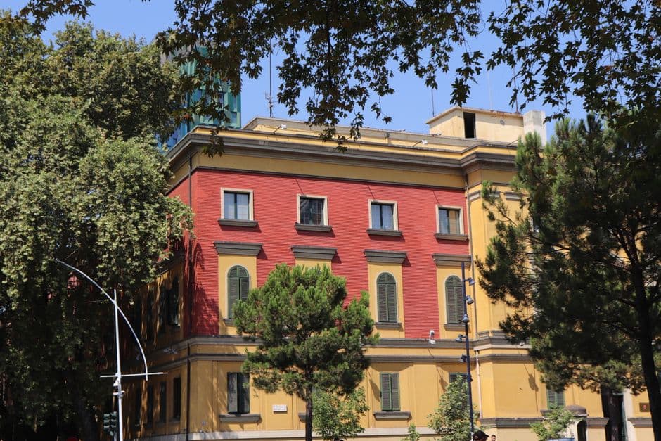 A vibrant red and yellow building surrounded by lush trees in an urban park.