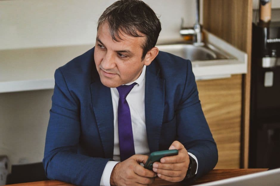 Professional man in office setting using smartphone, wearing a blue suit. Ideal for business or corporate themes.
