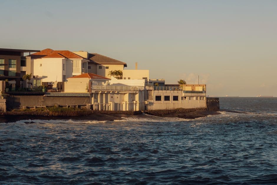 A serene view of a coastal Mediterranean style house by the sea during sunset, reflecting warm and calming tones.