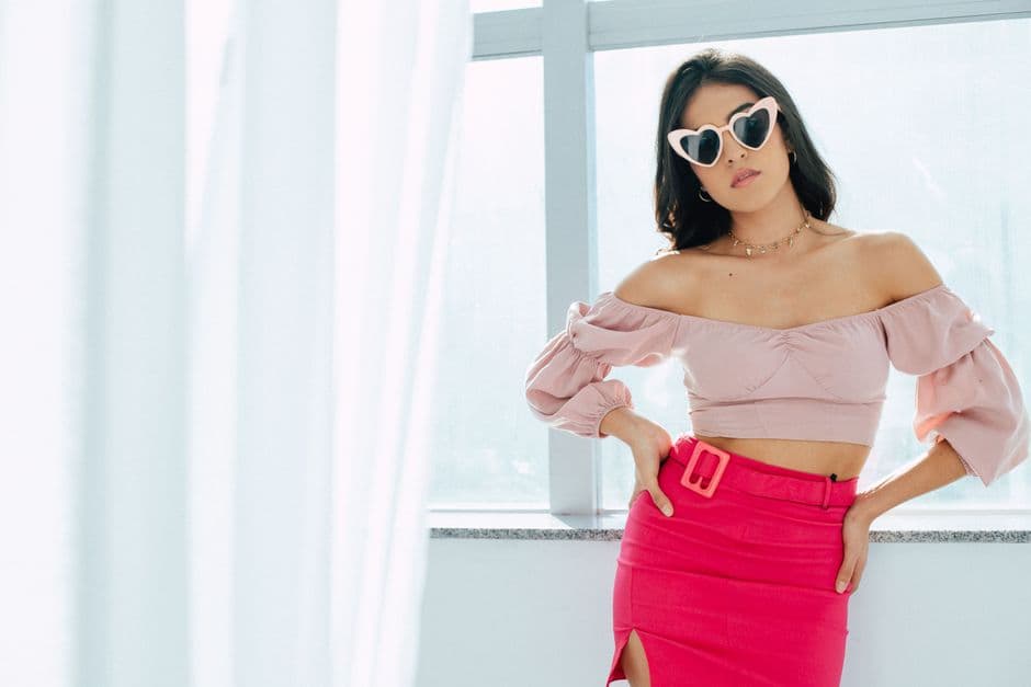 Stylish woman in trendy pink outfit with heart-shaped sunglasses posing indoors.