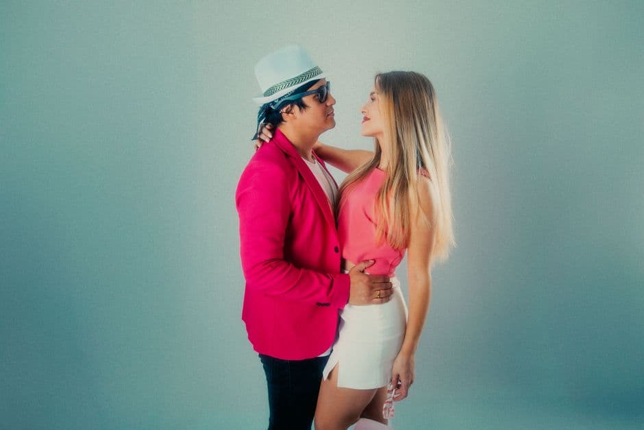 Elegant couple posing stylishly, wearing pink outfits against a neutral background.