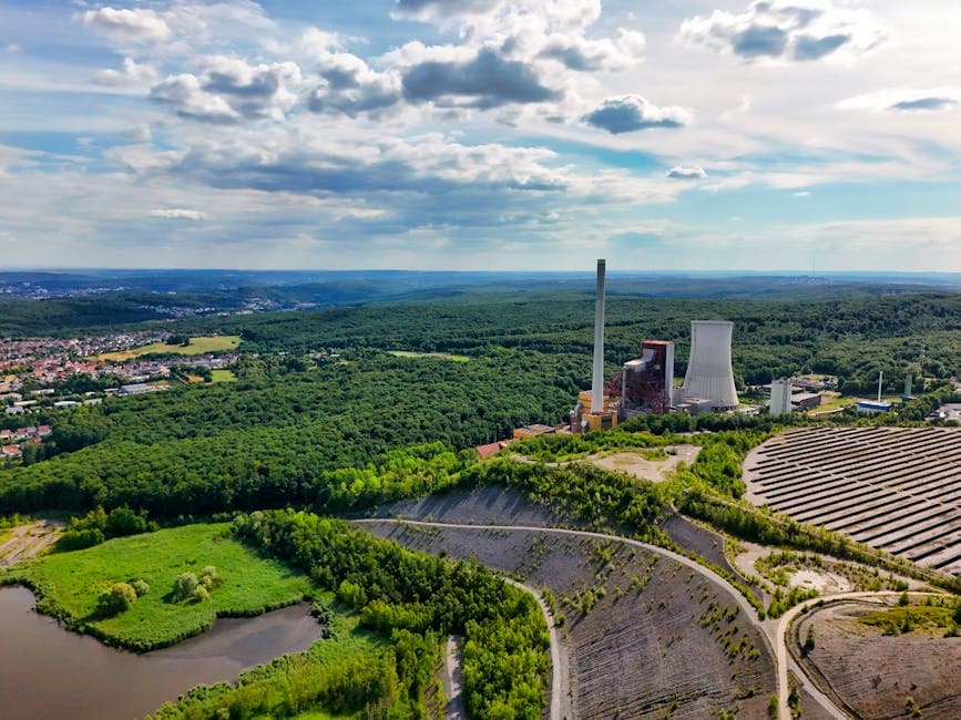 Aerial view of power plant surrounded by forests and clear skies, capturing nature-industry contrast.