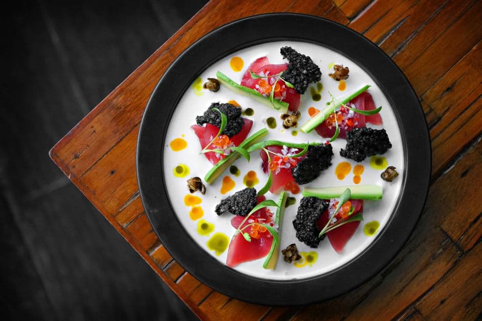 Elegant gourmet dish featuring black caviar and tuna with vibrant garnish served on a wooden table.