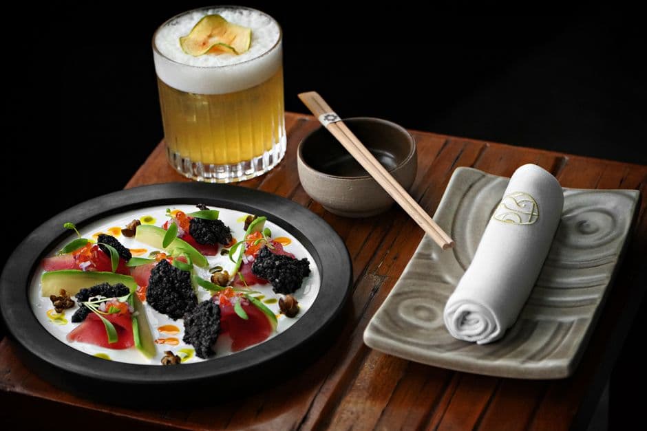 Exquisite Peruvian-Japanese fusion dish with a fresh cocktail, beautifully presented on wooden table.