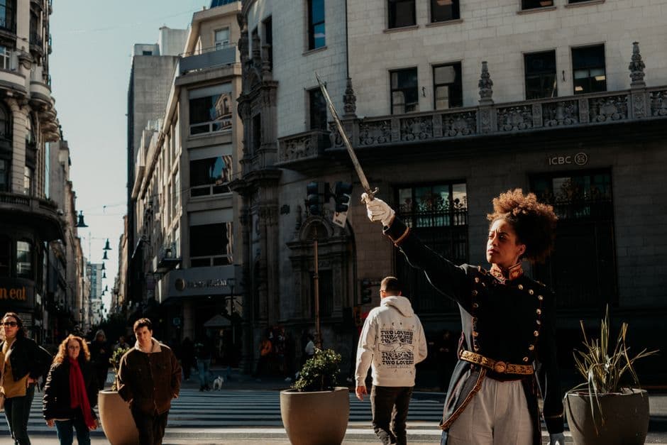 A street performer in traditional attire poses with a sword in Buenos Aires under bright daylight.