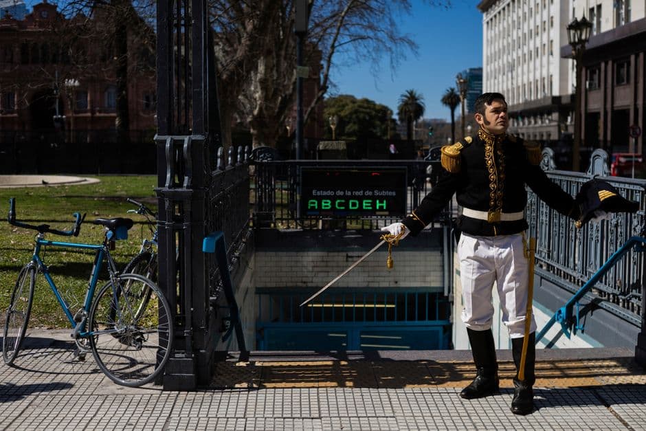 A man in historical uniform gesturing outside a subway entrance in Buenos Aires.