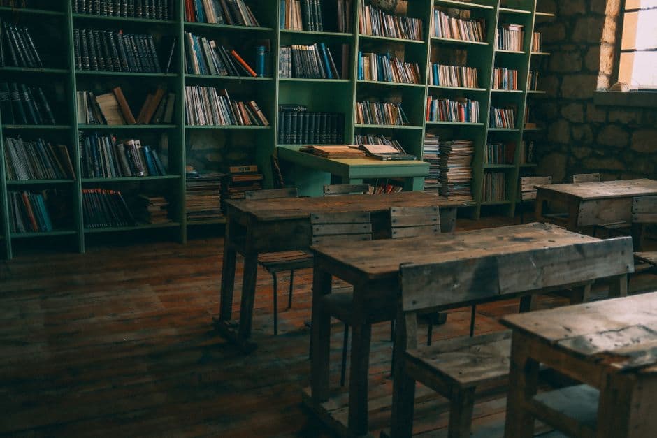 A rustic, vintage classroom featuring wooden desks and bookshelves filled with books.