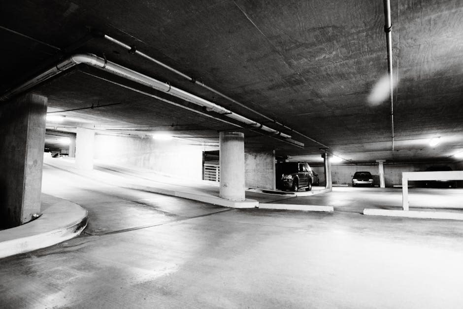 Black and white photo of a spacious underground parking garage with cars parked and concrete pillars.